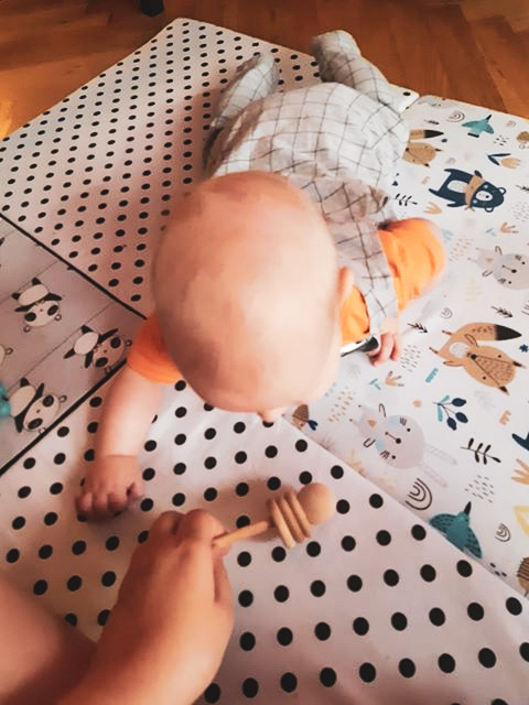 niemowlę bawi się drewnianą zabawką na macie